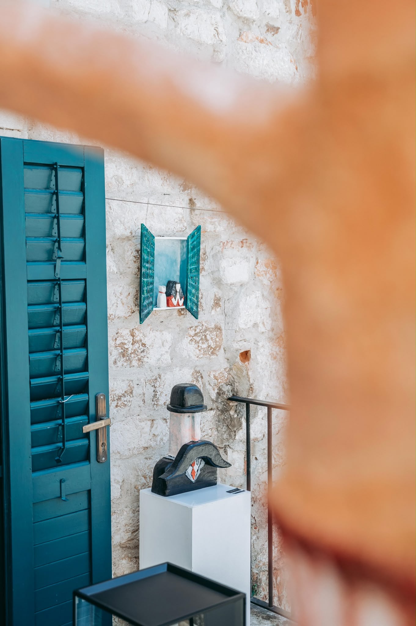 Two figurative sculptures framed by green shutters in a stone building