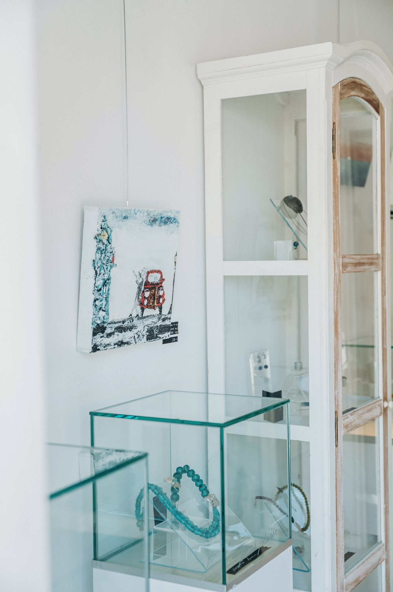 A turquoise handmade grasshopper sculpture on a white gallery pedestal